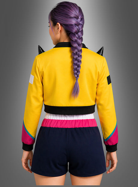 Eine Person mit violett geflochtenen Haaren, gekleidet im K-Pop-Romy-Outfit für Damen mit Jacke – bestehend aus einer gelben Jacke mit schwarzen Akzenten und marineblauen Shorts mit rosa Bund –, steht mit dem Rücken zur Kamera und präsentiert dieses auffällige Ensemble.