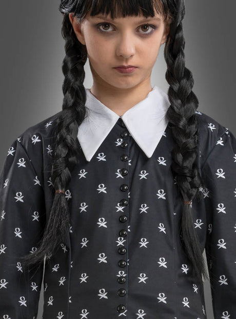 Ein Mädchen mit langen, schwarzen Zöpfen, das das „Wednesday Mädchen Kleid schwarz-weiß“ trägt – ein schwarzes Kleid mit weißem Kragen und Totenkopfmotiven –, steht vor einem grauen Hintergrund und erinnert dabei an den charakteristischen Stil des Wednesday-Kostüms aus der Addams Family.