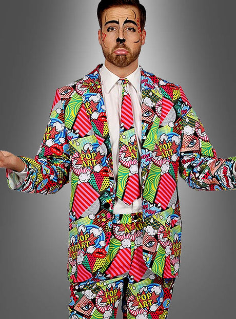 Ein Mann trägt den „Pop Art Anzug für Herren“ mit einem farbenfrohen Design im Comic-Stil, einer passenden Krawatte und einer von Comics inspirierten Gesichtsbemalung; er steht mit leicht ausgestreckten Armen und einem neutralen Gesichtsausdruck vor einem grauen Hintergrund.