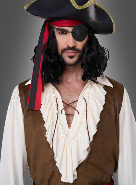 Vor einem grauen Hintergrund steht ein Mann, der eine Piratenverkleidung für Herren trägt, bestehend aus einem schwarzen Hut, einem roten Bandana, einer Augenklappe, einer langen schwarzen Perücke, einem weißen Hemd mit Rüschen und einer braunen Weste.