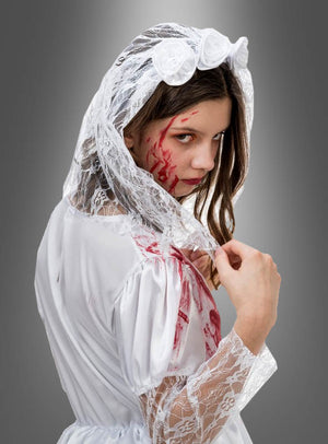 Ein Mädchen trägt das „Blutige Braut Carmilla“-Kinderkostüm, bestehend aus einem weißen Brautkleid aus Spitze und einem Schleier, mit auffälligen Kunstblutspuren im Gesicht und auf der Schulter, was für einen gruseligen Halloween-Look sorgt. Sie blickt vor einem grauen Hintergrund über die Schulter – damit ist dieses Kostüm die perfekte Inspiration für gruselige Kinderkostüme.