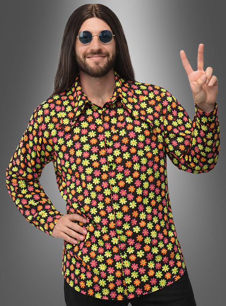 Eine Person, die ein farbenfrohes Deluxe-Blumenhemd im Hippie-Stil für Herren trägt, mit langen dunklen Haaren und einer runden Sonnenbrille, formt mit einer Hand ein Peace-Zeichen vor einem schlichten Hintergrund mit Farbverlauf.