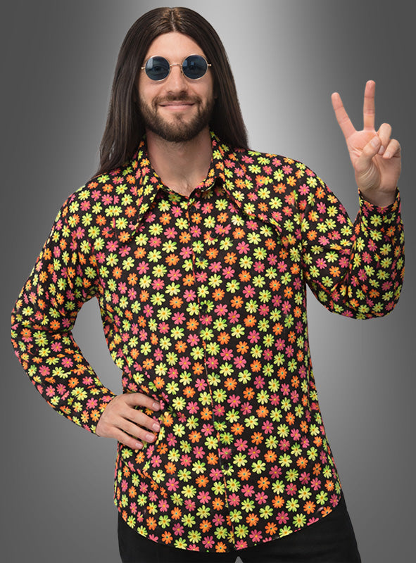 Eine Person, die ein farbenfrohes Deluxe-Blumenhemd im Hippie-Stil für Herren trägt, mit langen dunklen Haaren und einer runden Sonnenbrille, formt mit einer Hand ein Peace-Zeichen vor einem schlichten Hintergrund mit Farbverlauf.