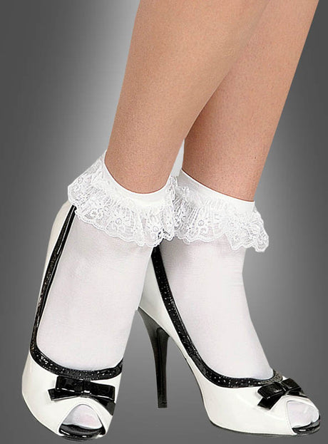 Eine Person, die weiße Socken mit Spitze und schwarz-weiße Schuhe mit hohen Absätzen und Schleifen trägt und vor einem grauen Hintergrund steht, vermittelt den Eindruck eines verspielten Rock’n’Roll-Kostüms.
