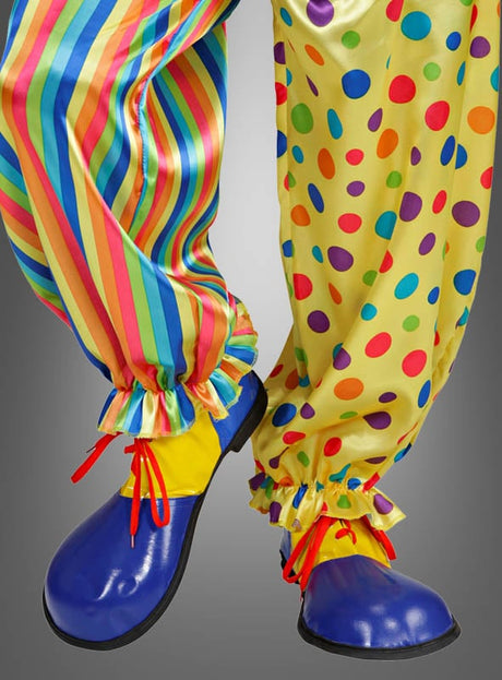 Eine Person, die übergroße Clownschuhe für Erwachsene und eine Clownshose trägt – ein Hosenbein mit Regenbogenstreifen, das andere mit gelben und bunten Punkten –, steht vor einem grauen Hintergrund und rundet damit ihr farbenfrohes Clownskostüm ab.