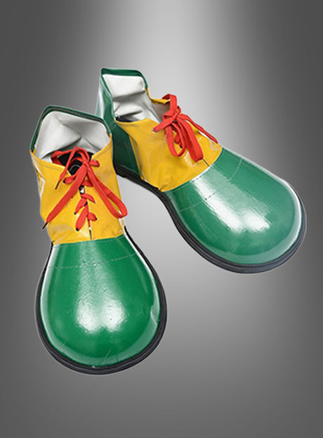 Ein Paar Clown-Schuhe für Erwachsene im Oversize-Design mit grünen Schuhspitzen, gelben Seiten und roten Schnürsenkeln ist vor einem grauen Hintergrund mit Farbverlauf abgebildet.