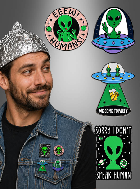 Ein Mann mit einer Alufolienmütze und einer Jeansweste, die mit Metallabzeichen und Alien-Ansteckern verziert ist, bewundert die „Alien Pins Anstecker Weltall“-Kollektion, die illustrierte Alien-Motive mit Sprüchen wie „IIIIH! MENSCHEN!“ und „Tut mir leid, ich spreche kein Menschisch“ zeigt. Diese lustigen Anstecker verleihen seinem außergewöhnlichen Look eine skurrile Note.