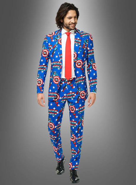 Ein Mann in einem blauen „Deluxe Captain America OppoSuit“-Anzug mit den ikonischen Schilden, einer roten Krawatte, einem weißen Hemd und schwarzen Schuhen steht vor einem grauen Hintergrund mit Farbverlauf.