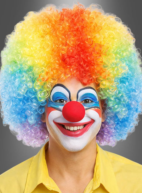 Eine als Clown verkleidete Person mit einer regenbogenfarbenen Lockenperücke, einer roten Nase, bunter Gesichtsbemalung und einem gelben Hemd, die in die Kamera lächelt. Die leuchtenden Riesen-Afro-Perücken in tollen Farben verleihen dem verspielten Look einen zusätzlichen Hauch von Spaß.