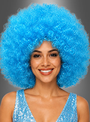 Eine Frau lächelt, während sie eine große, lockige, blaue XXL-Perücke mit der Aufschrift „Riesen Afro Perücken in tollen Farben“ und ein blaues Pailletten-Oberteil trägt; im Hintergrund ist ein neutrales Grau zu sehen.