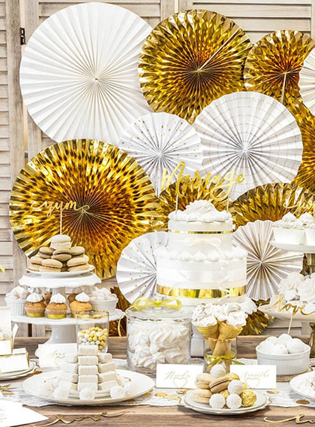 Desserttisch mit weißen und goldenen Torten, Macarons, Cupcakes und Süßigkeiten, im Hintergrund verziert mit großen gold-weißen „3“ aus Metallic-Papierfächer-Rosetten (23–40 cm) als elegante Partydekoration.