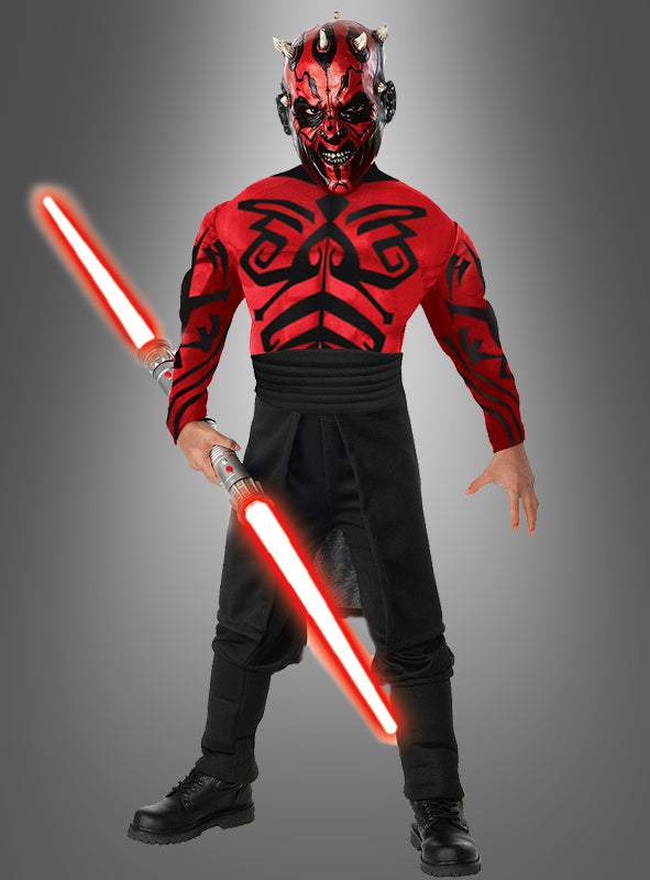 Eine Person in einem „Darth Maul Kinderkostüm Deluxe mit Muskeln“ und Gesichtsbemalung, die ein rot schwingendes Doppelklingen-Lichtschwert in der Hand hält und vor einem schlichten grauen Hintergrund steht – perfekt für Star-Wars-Fans und Kinder, die diese Kultfigur zum Leben erwecken möchten.