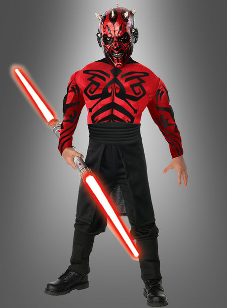 Eine Person in einem „Darth Maul Kinderkostüm Deluxe mit Muskeln“ und Gesichtsbemalung, die ein rot schwingendes Doppelklingen-Lichtschwert in der Hand hält und vor einem schlichten grauen Hintergrund steht – perfekt für Star-Wars-Fans und Kinder, die diese Kultfigur zum Leben erwecken möchten.