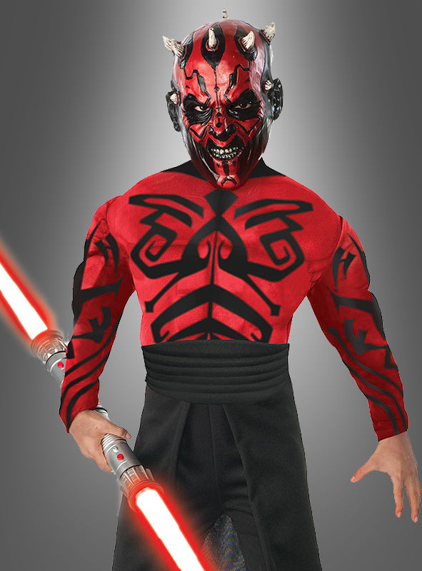 Ein Kind im Darth-Maul-Kinderkostüm Deluxe mit Muskeln, komplett mit Gesichtsbemalung und einem roten Doppelklingen-Lichtschwert in der Hand, steht vor einem grauen Hintergrund mit Farbverlauf und erinnert an die ikonische „Star Wars“-Figur.
