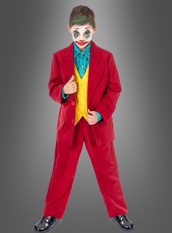 Ein Kind, das den „Roten Joker-Anzug für Kinder“ trägt – bestehend aus einem roten Anzug, einer gelben Weste, einem blaugrünen Hemd und einer Clown-ähnlichen Gesichtsbemalung –, steht vor einem grauen Hintergrund.