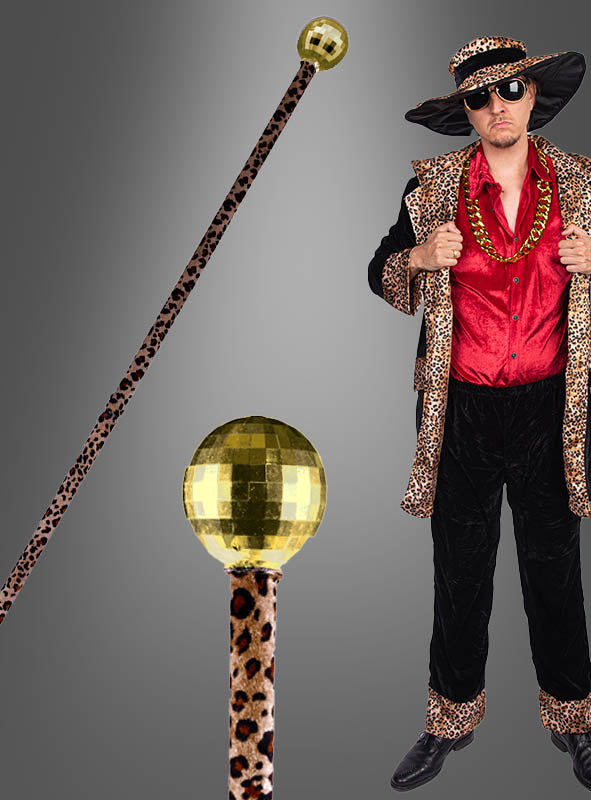 Vor einem grauen Hintergrund steht ein Mann, der ein Kostüm im Leopardenmuster „Gehstock Macho Pimp in Zebra oder Leo 96 cm“ trägt, einen goldenen Disco-Kugel-Spazierstock in der Hand hält und ein rotes Hemd, eine Sonnenbrille, eine goldene Kette sowie einen breitkrempigen Hut trägt.