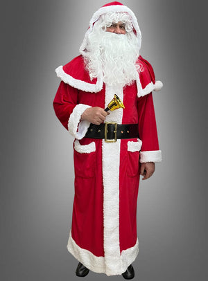 Eine Person, die einen Weihnachtsmann-Mantel mit Stiefelüberzügen trägt, einen weißen Bart und ein rotes Plüschkostüm hat und eine kleine goldene Glocke in der Hand hält, während sie vor einem grauen Hintergrund steht.