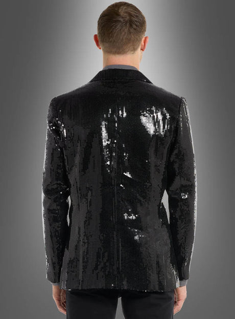 Eine Person steht mit dem Rücken zur Kamera und trägt die „Pailletten Jackett Herren Schwarz“ aus glänzenden schwarzen Pailletten sowie eine dazu passende schwarze Hose vor einem grauen Hintergrund mit Farbverlauf.