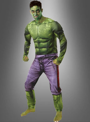 Eine Person, die das „Hulk-Kostüm für Herren von Marvel“ trägt – bestehend aus einem grünen Muskelanzug und einer violetten Hose –, posiert barfuß als Hulk vor einem schlichten Hintergrund mit Farbverlauf.