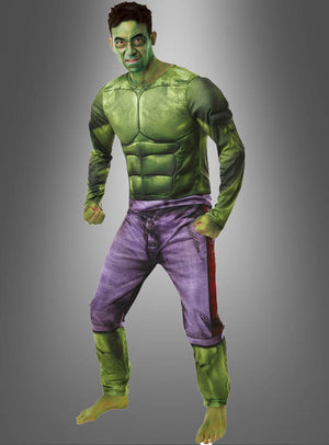 Eine Person, die das „Hulk-Kostüm für Herren von Marvel“ trägt – bestehend aus einem grünen Muskelanzug und einer violetten Hose –, posiert barfuß als Hulk vor einem schlichten Hintergrund mit Farbverlauf.