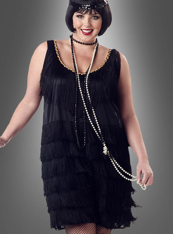 Eine Frau lächelt in einem schwarzen XXL-Charleston-Kleid mit Fransen, das von der Mode der 20er Jahre inspiriert ist und mit langen Perlenketten, Netzstrümpfen und einem mit Perlen verzierten Stirnband geschmückt ist, während sie vor einem grauen Hintergrund mit Farbverlauf posiert.