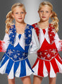 Zwei junge Mädchen mit blonden Zöpfen tragen passende Cheerleader-Outfits für Mädchen – das eine in Blau und Weiß, das andere in Rot und Weiß – und stehen nebeneinander vor einem grauen Hintergrund.