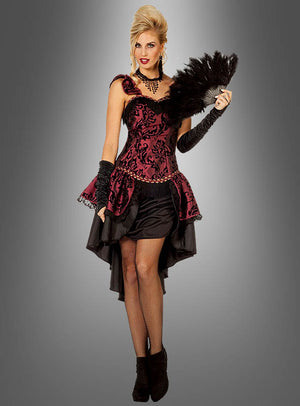 Eine Frau in einem verführerischen roten Burlesque-Kleid, kombiniert mit Netzstrümpfen, schwarzen Handschuhen und einem Federfächer, vor einem grauen Hintergrund mit Farbverlauf – ein glamouröser Karnevalslook für Damen mit einem eleganten Korsagenkleid.