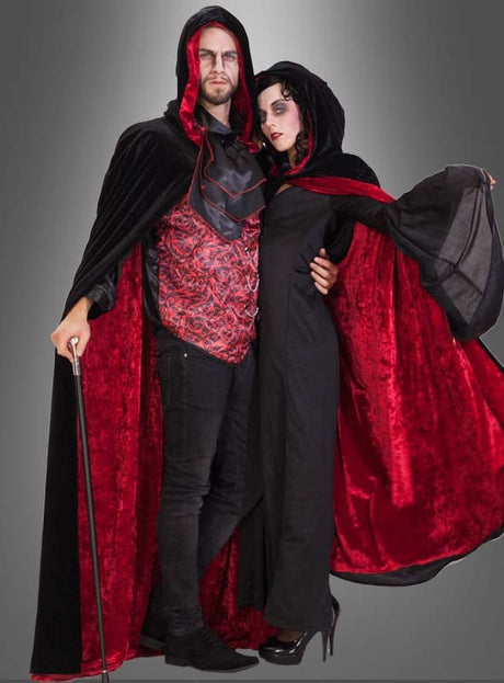 Zwei Personen in identischen schwarzen und roten „Premium Kapuzen Wendecape Unisex“-Capes stehen gemeinsam vor einem schlichten grauen Hintergrund.
