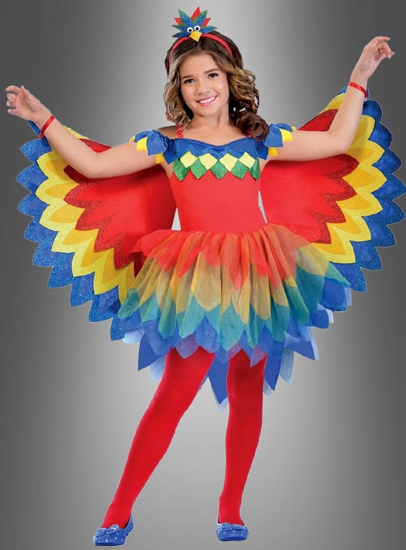 Ein Kind posiert in einem farbenfrohen Paradiesvogel-Papagei-Kostüm für Mädchen mit leuchtend roten, gelben, blauen und grünen Flügeln, einem passenden Stirnband und roten Strumpfhosen vor einem grauen Hintergrund mit Farbverlauf – perfekt als Kinderfasching-Kostüm oder Paradiesvogel-Kostüm für festliche Anlässe.