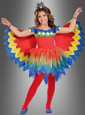 Ein Kind posiert in einem farbenfrohen Paradiesvogel-Papagei-Kostüm für Mädchen mit leuchtend roten, gelben, blauen und grünen Flügeln, einem passenden Stirnband und roten Strumpfhosen vor einem grauen Hintergrund mit Farbverlauf – perfekt als Kinderfasching-Kostüm oder Paradiesvogel-Kostüm für festliche Anlässe.