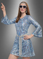 In einem 70er-Jahre-Disco-Kleid-Outfit mit Accessoires – bestehend aus einem funkelnden, blau gemusterten Kleid, einem silbernen Gürtel, einer übergroßen Sonnenbrille und einem passenden Stirnband – nimmt eine Frau vor einem grauen Hintergrund mit Farbverlauf eine klassische Disco-Pose ein: einen Arm erhoben und den Finger nach oben gerichtet. Dieses Ensemble ist die ideale Wahl für jedes 70er-Jahre-Outfit oder jeden Disco-Kostüm-Stil für Damen.