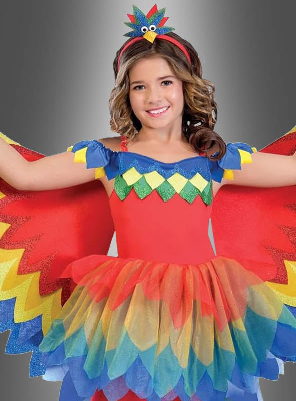 Ein Kind posiert mit ausgestreckten Armen vor einem grauen Hintergrund. Es trägt das farbenfrohe „Paradiesvogel-Papagei-Kostüm für Mädchen“ mit gefiederten Flügeln, einem bunten Tutu und einem passenden Stirnband – die ideale Wahl für den Kinderfasching als auffälliges Paradiesvogel-Kostüm.