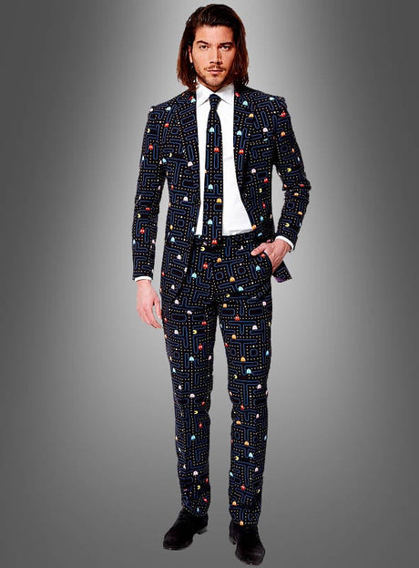 Ein Mann, gekleidet im „Deluxe Pac-Man-Anzug“ von Opposuits – einem auffälligen schwarzen Anzug mit Krawatte und Hose, verziert mit einem markanten Pac-Man-Muster –, steht vor einem grauen Hintergrund mit Farbverlauf, eine Hand in der Tasche, und strahlt den selbstbewussten Stil eines Arcade-Zockers aus.