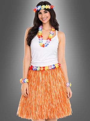Eine Frau steht lächelnd vor einem grauen Hintergrund und trägt ein weißes Trägertop sowie das 5-teilige Hawaii-Set mit Rock und Accessoires, zu dem ein orangefarbener Grasrock und bunte Blumen-Accessoires gehören.