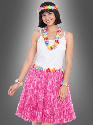 Eine Frau, die ein weißes Trägertop, einen rosa Grasrock und bunte Blumenaccessoires aus dem 5-teiligen Hawaii-Set mit Rock & Accessoires trägt, steht lächelnd vor einem grauen Hintergrund.