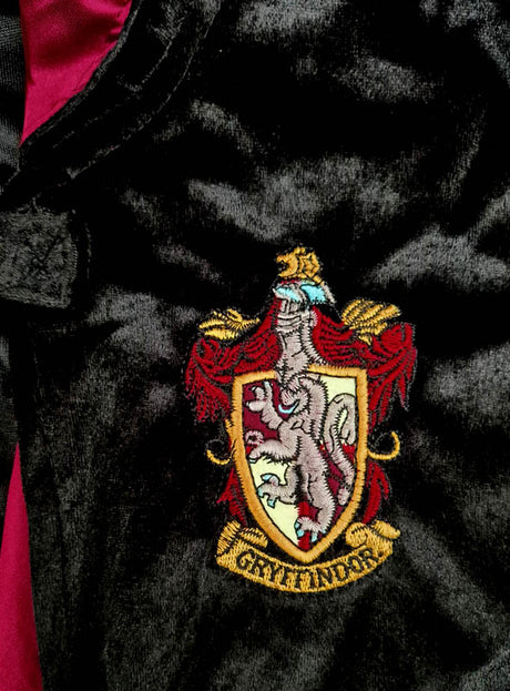 Nahaufnahme eines Gryffindor-Wappenaufnähers auf dunklem Stoff, der beim „Harry Potter Kostüm Gryffindor Deluxe“ zu sehen ist – einer authentischen Robe mit einem Löwenwappen und dem in Goldbuchstaben geschriebenen Hausnamen, perfekt für jedes Harry-Potter-Kostüm.