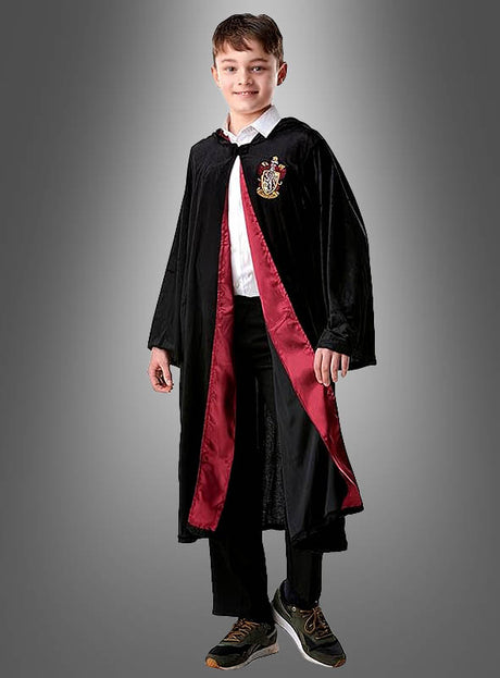 Ein Junge, der das Harry-Potter-Kostüm „Gryffindor Deluxe“ mit rotem Futter und Wappen trägt, steht mit dem Gesicht nach vorne und lächelt vor einem schlichten grauen Hintergrund.