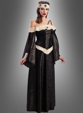 Vor einem grauen Hintergrund steht eine Frau, die das mittelalterliche Damenkleid „Edelfrau Mechthild“ trägt, ein schwarz-cremefarbenes Kleid im mittelalterlichen Stil mit ausgestellten Ärmeln und einem passenden, verzierten Stirnband.