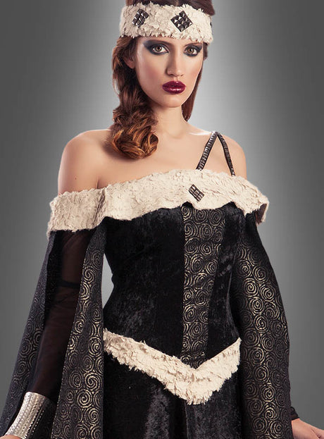 Eine Frau, die das „Mittelalterliches Damenkleid Edelfrau Mechthild“ trägt – ein mittelalterlich inspiriertes, schwarz-cremefarbenes Kleid mit gemusterten Ärmeln und einem passenden Stirnband –, posiert vor einem grauen Hintergrund mit Farbverlauf.