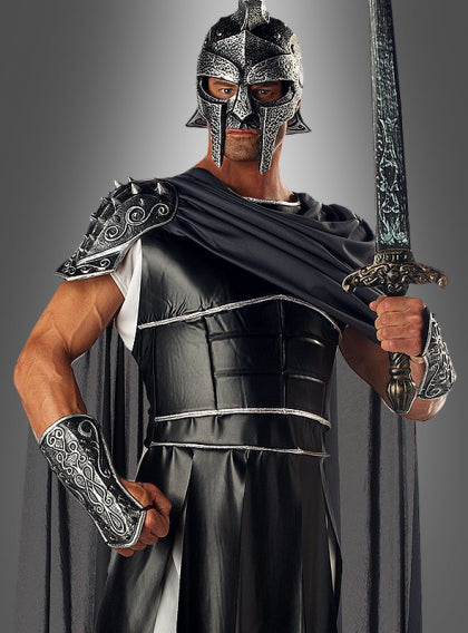 Eine Person in einer schwarz-silbernen Rüstung und einem Helm im griechischen Stil hält ein Schwert aufrecht in der Hand und blickt vor sich hin, vor einem schlichten, grauen Hintergrund.