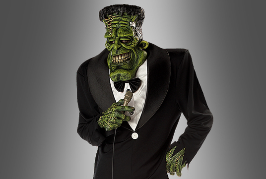 Eine Person in einem schwarzen Smoking und mit Fliege trägt eine grüne Frankenstein-Monster-Maske und Handschuhe und hält ein Mikrofon in der Hand, vor einem grauen Hintergrund mit Farbverlauf.