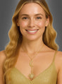 Eine lächelnde Frau mit langen blonden Haaren trägt ein goldenes Kleid und die goldfarbene Halskette „Sonne und Mond“ mit einem Anhänger in Form eines Halbmondes und eines Sonnenstrahlenmusters und posiert vor einem schlichten grauen Hintergrund.