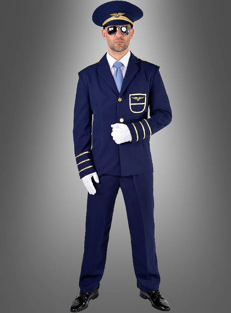 Ein Mann, der ein blaues „Pilot“-Kostüm für Herren mit goldenen Verzierungen, weiße Handschuhe, eine Sonnenbrille und einen passenden Hut trägt, steht vor einem grauen Hintergrund mit Farbverlauf.