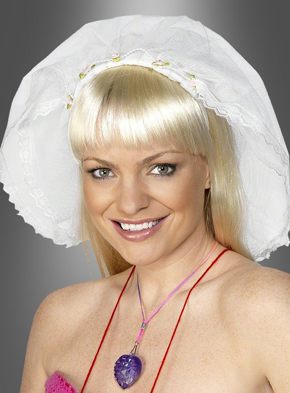 Eine lächelnde Person mit langen blonden Haaren trägt den „Brautschleier für Junggesellinnenabschied“ – eine weiße Haube mit Spitzenbesatz – sowie eine Halskette mit einem violetten, herzförmigen Anhänger, vor einem grauen Hintergrund.