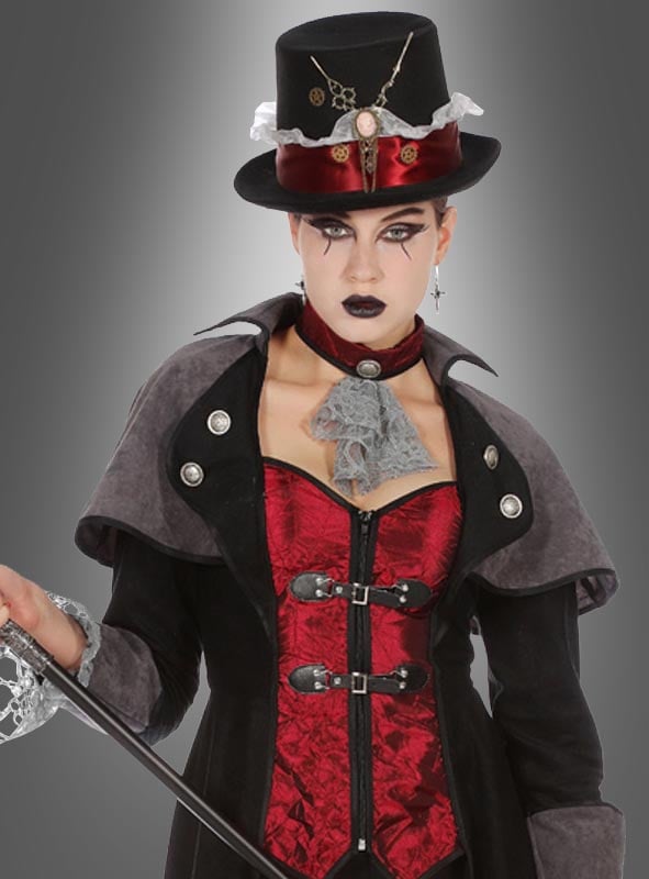 Eine Person in einem Gothic-Steampunk-Outfit mit schwarzem Zylinder, rotem Korsett, schwarzem Umhang und Spitzenhalsband, die einen Spazierstock in der Hand hält und vor einem grauen Hintergrund mit Farbverlauf steht. Abgerundet wird das auffällige Ensemble durch den dramatischen „Vampir Gothic Mantel Lady Demona“, der dem Look eine elegante Note verleiht.