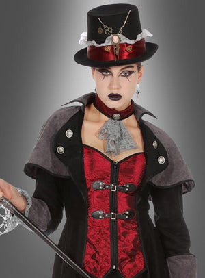 Eine Person in einem Gothic-Steampunk-Outfit mit schwarzem Zylinder, rotem Korsett, schwarzem Umhang und Spitzenhalsband, die einen Spazierstock in der Hand hält und vor einem grauen Hintergrund mit Farbverlauf steht. Abgerundet wird das auffällige Ensemble durch den dramatischen „Vampir Gothic Mantel Lady Demona“, der dem Look eine elegante Note verleiht.