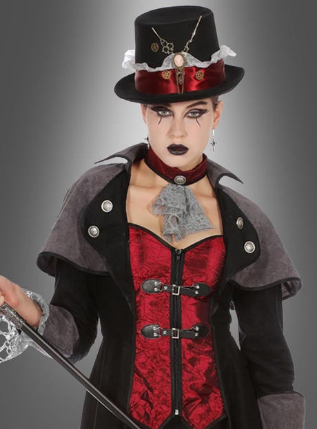 Eine Person in einem Gothic-Steampunk-Outfit mit schwarzem Zylinder, rotem Korsett, schwarzem Umhang und Spitzenhalsband, die einen Spazierstock in der Hand hält und vor einem grauen Hintergrund mit Farbverlauf steht. Abgerundet wird das auffällige Ensemble durch den dramatischen „Vampir Gothic Mantel Lady Demona“, der dem Look eine elegante Note verleiht.