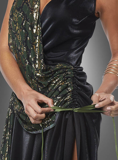 Eine Person, die das Medusa-Schlangenkostüm für Damen trägt – mit einem glänzenden schwarz-grünen Muster –, bindet sich ein grünes Band um die Taille, sodass nur ihr Oberkörper und ihre Hände zu sehen sind.