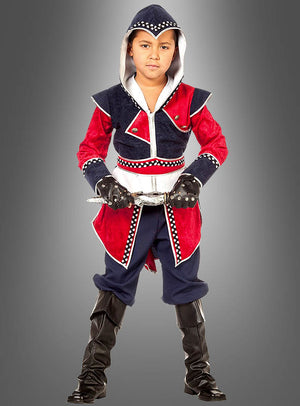 Ein Kind, das das „Fantasy Krieger“-Kinderkostüm trägt – ein rot-marineblaues Outfit im Assassinen-Stil mit Kapuze, Handschuhen, Gürtel und schwarzen Stiefeln –, steht vor einem grauen Hintergrund.