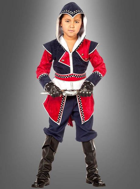 Ein Kind, das das „Fantasy Krieger“-Kinderkostüm trägt – ein rot-marineblaues Outfit im Assassinen-Stil mit Kapuze, Handschuhen, Gürtel und schwarzen Stiefeln –, steht vor einem grauen Hintergrund.